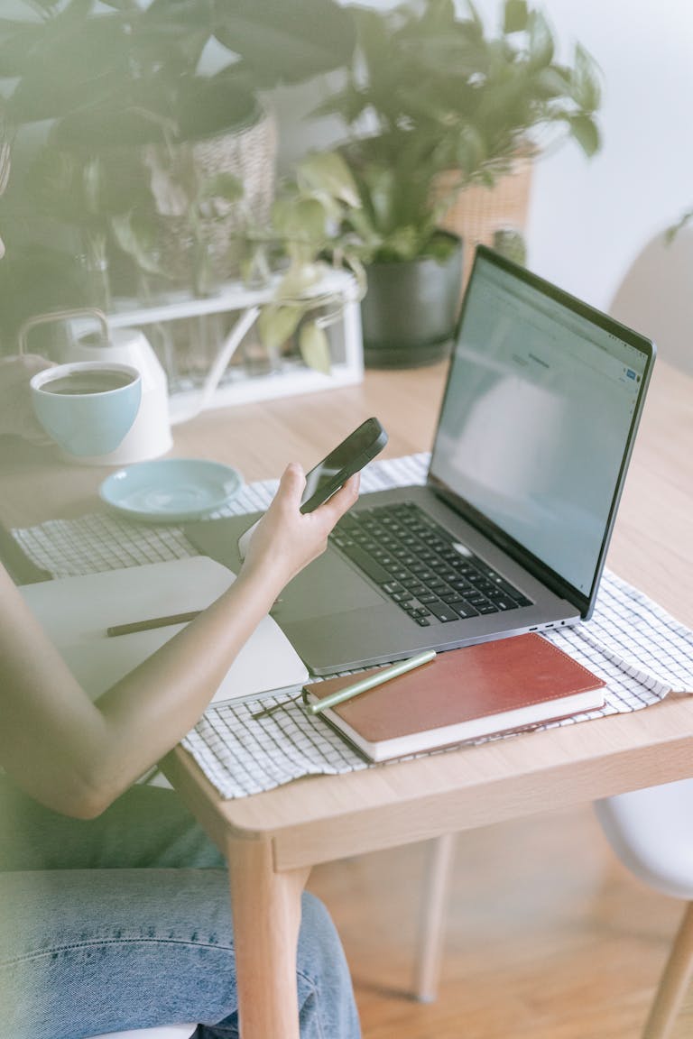 A woman works remotely using a laptop and smartphone in a stylish indoor setup.